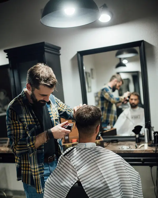 Barbero cortando el cabello a un cliente frente al espejo del local